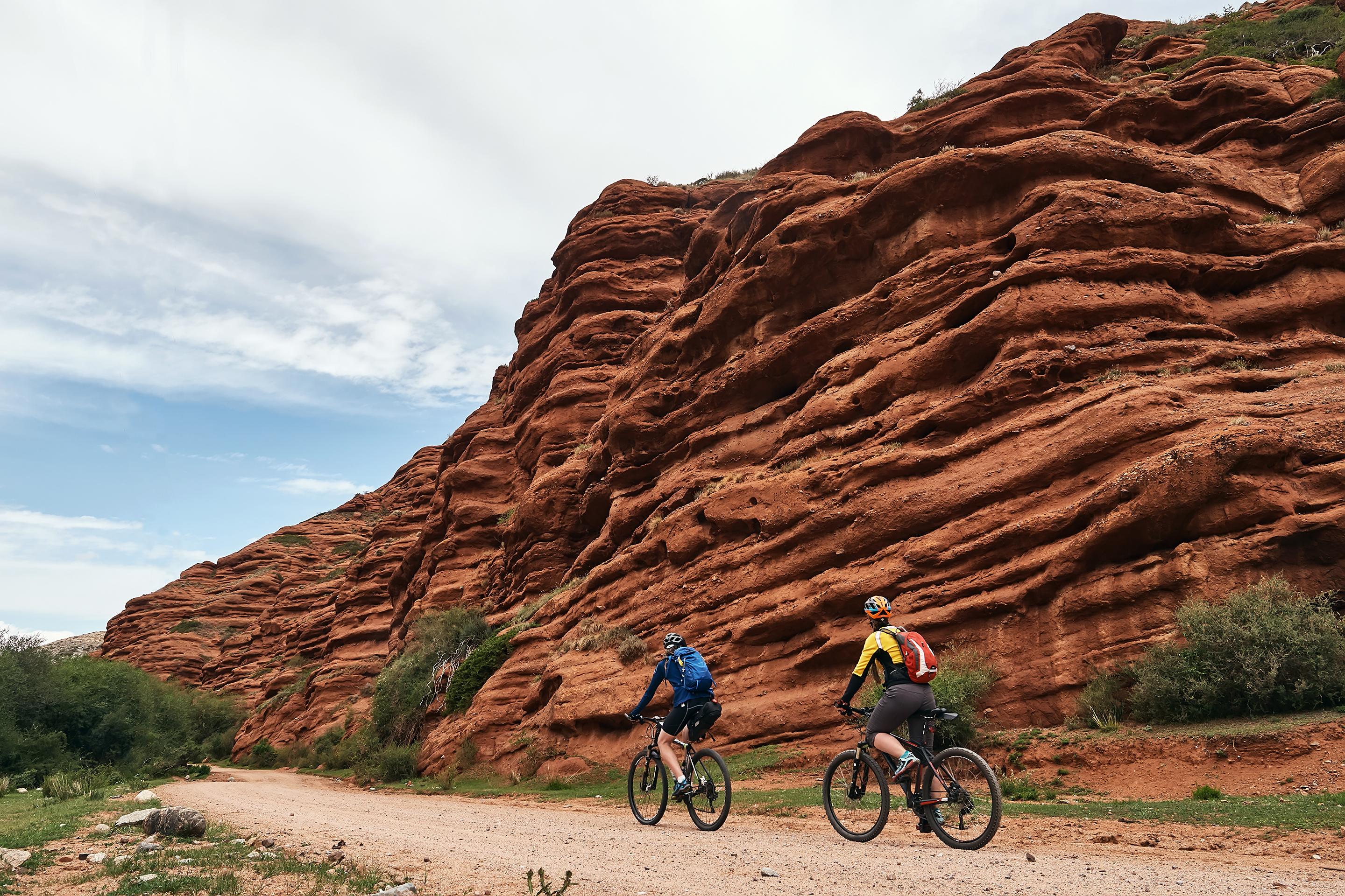 Two cyclist riding along the Amazing Red Mountain range of Jeti Oguz (Seven bulls Rock Canyon) Kyrgyzstan